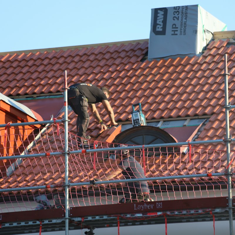 Couvreur au travail sur un toit en tuiles rouges, derrière un échafaudage