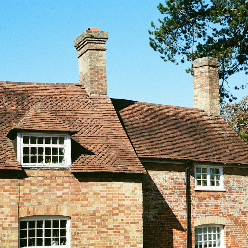 Maison en brique à toit de tuiles en terre cuite, avec lucarne blanche et cheminées